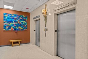 An elevator area with a modern design, including a wall-mounted light fixture and a colorful abstract painting. - Caribbean Sea View | Tmobile District Free Parking (SanJuan)