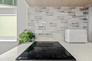 A modern kitchen with a black induction cooktop, a white built-in oven, and a backsplash with rectangular tiles. - Caribbean Sea View | Tmobile District Free Parking (SanJuan)