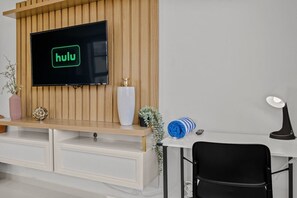 Een moderne kamer met een aan een houten muur bevestigde televisie, een bureau met stoel, en diverse decoratieve objecten.