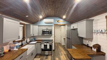 A compact kitchen with wooden flooring, white cabinetry, a stainless steel oven, and a microwave.