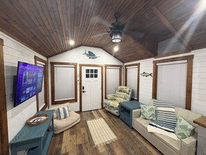 A cozy room with a television, a ceiling fan, a couch, and a chair.