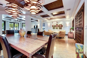 Uma sala de jantar espaçosa com uma mesa de madeira comprida, várias cadeiras e um lustre moderno.