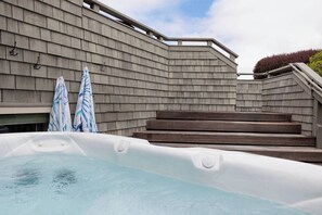 A hot tub with steps leading up to it, a wooden wall, and two striped umbrellas. - Coastal retreat with game room, hot tub & more (Bodega Bay)