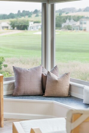 A corner window with a view of a green field and buildings. There are several cushions on the window sill. - Coastal retreat with game room, hot tub & more (Bodega Bay)