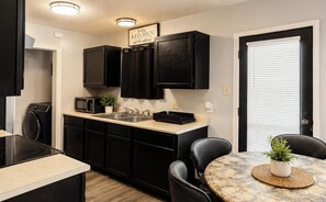 A compact kitchen with black cabinets, a microwave, and a sink. There is a dining area with a table and chairs. - Cozy 2-bedroom house in gorgeous Lubbock (Lubbock)