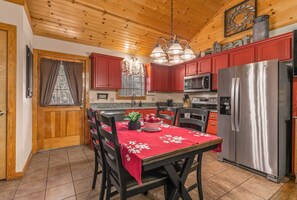 A kitchen with wooden ceiling, red cabinets, stainless steel appliances, and a dining table with a red tablecloth. - Pet Friendly Resort Cabin, Branson Woods, Indoor Pool! Luxury Sleeper! | 10 (Branson)