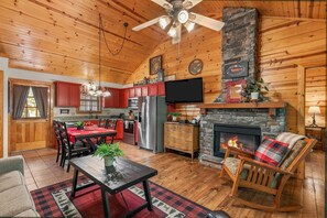 A log cabin interior with a dining area, kitchen, fireplace, and a ceiling fan. - Pet Friendly Resort Cabin, Branson Woods, Indoor Pool! Luxury Sleeper! | 10 (Branson)