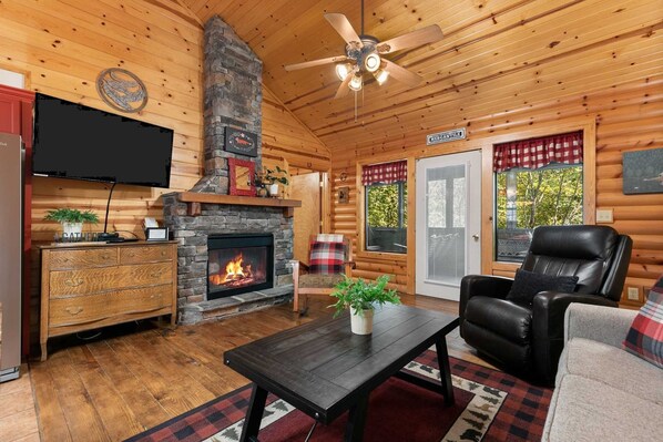 A log cabin interior with a fireplace, a television, a leather chair, and a dining table. - Pet Friendly Resort Cabin, Branson Woods, Indoor Pool! Luxury Sleeper! | 10 (Branson)