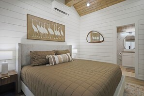 Ein Schlafzimmer mit einem großen Bett, einem Kopfteil, einem Wandbild mit Vögeln, einem Spiegel und einer Holzbalkendecke.