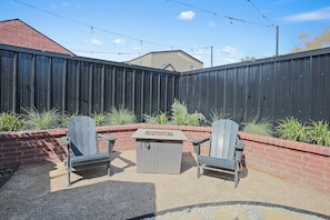 Eine Terrassenausstattung mit zwei Adirondack-Stühlen, einem quadratischen Tisch und einem Pflanzkübel aus Ziegelsteinen mit Pflanzen.