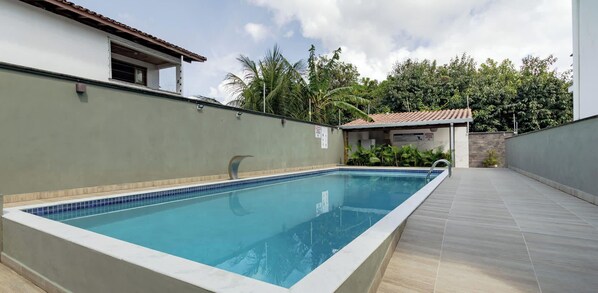 Ein rechteckiger Swimmingpool mit einer gefliesten Kante, umgeben von einer gefliesten Liegefläche und einer niedrigen Mauer.