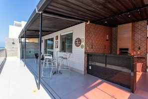 A rooftop terrace with a covered seating area, a bar, and a patterned wall. - Cobertura a 40m da Praia do Morro c Churrasqueira (Luis Correia)