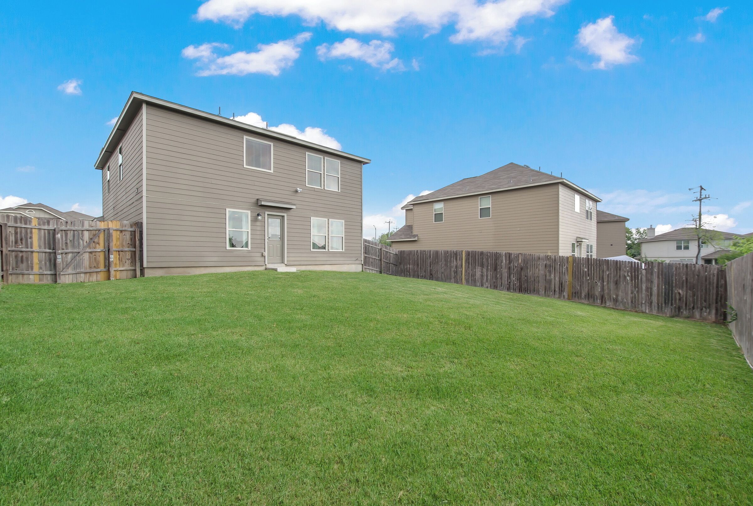 A two-story residential building with a fenced backyard and a clear sky.