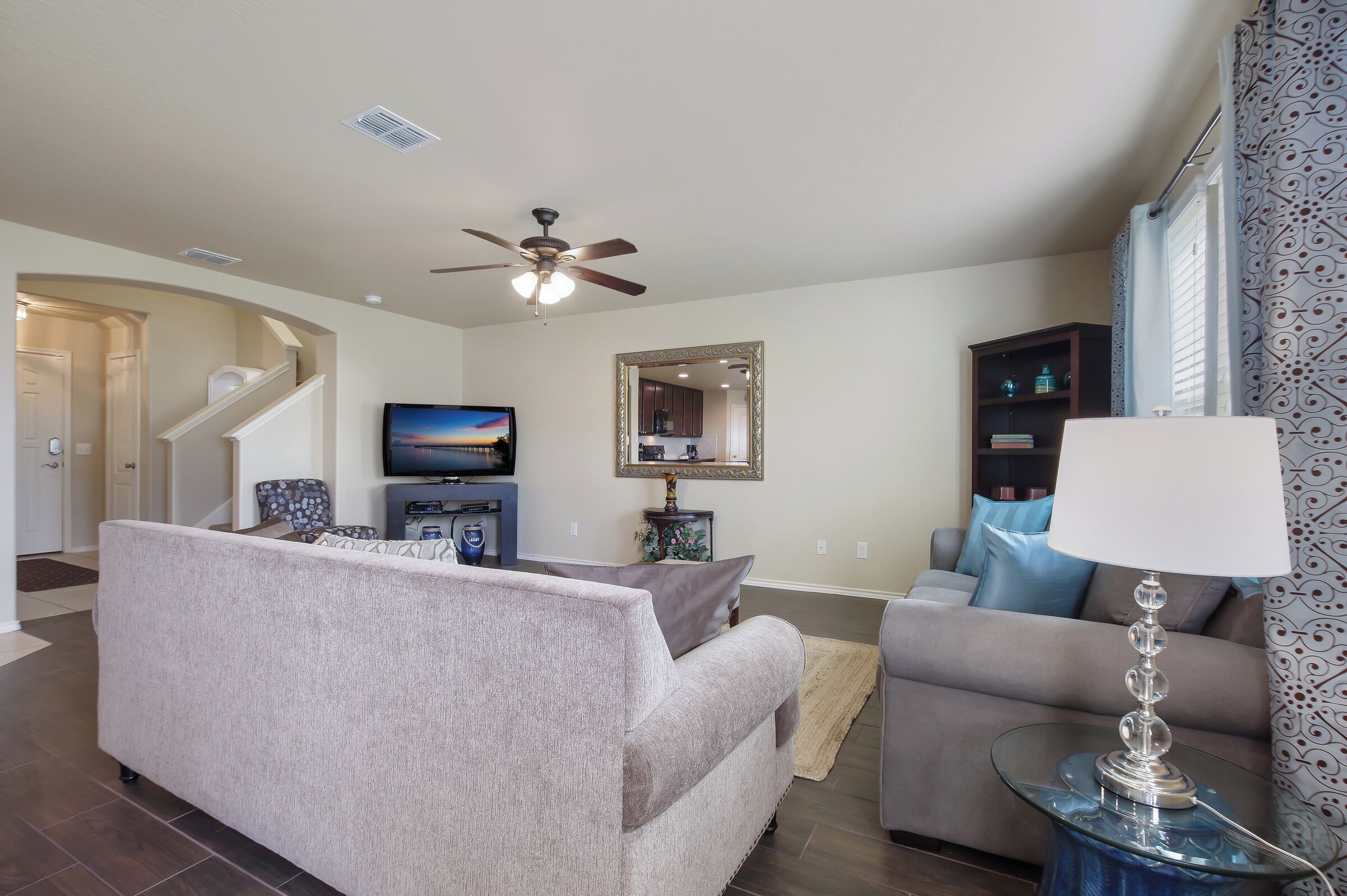 A living room with a sofa, a television, a ceiling fan, and a dining area with a table and chairs.