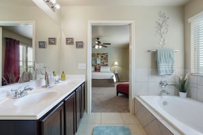 Une salle de bain avec deux lavabos, une baignoire, un ventilateur de plafond et un miroir.