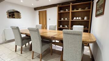 A dining area with a wooden table and grey upholstered chairs, a wooden bookshelf with tea sets, and a white radiator.
