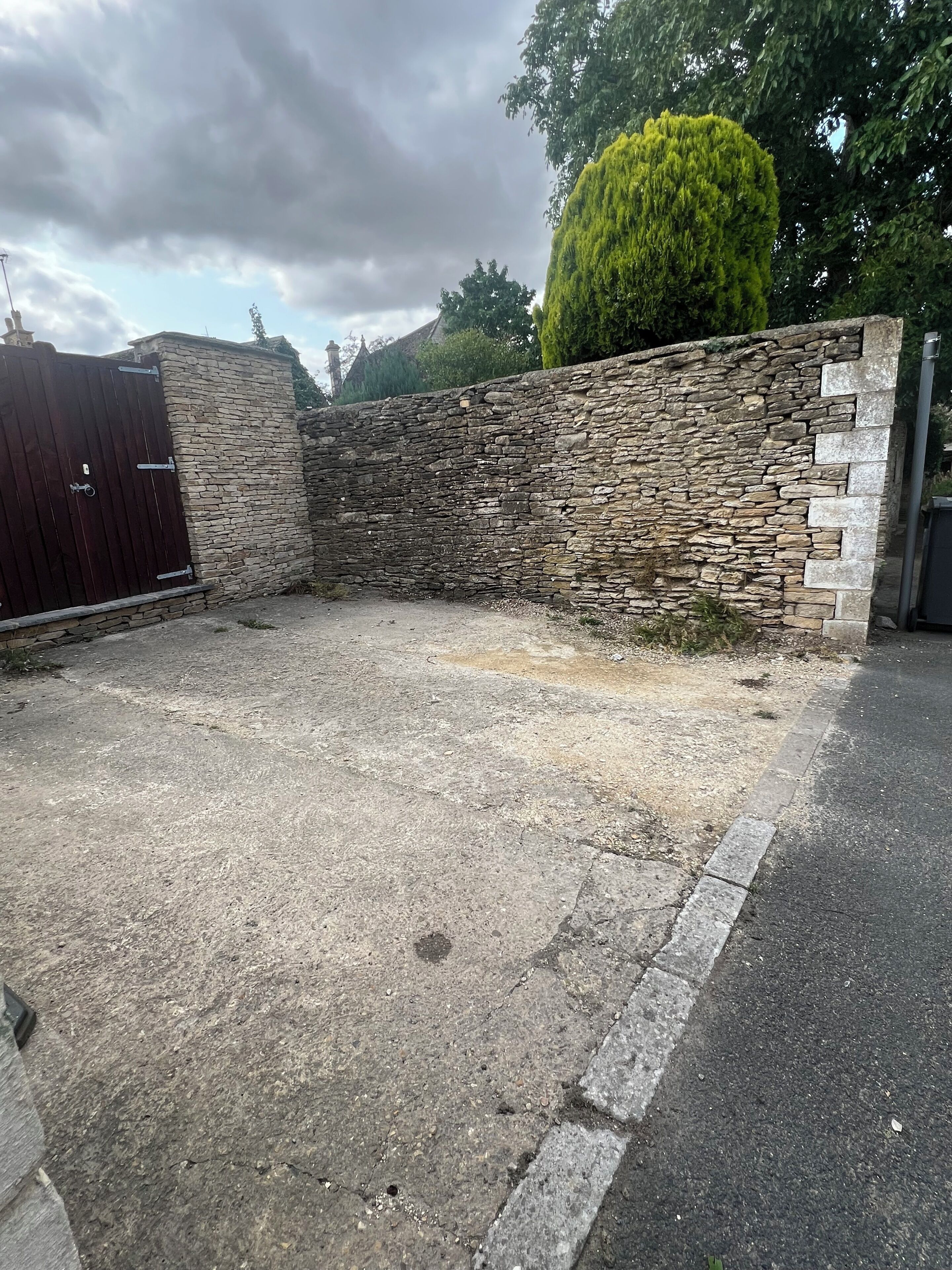 Un área pavimentada con un muro de piedra y una puerta metálica.