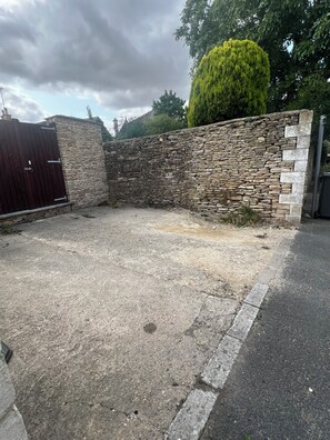 Una zona pavimentada amb un mur de pedra i una reixa metàl·lica.