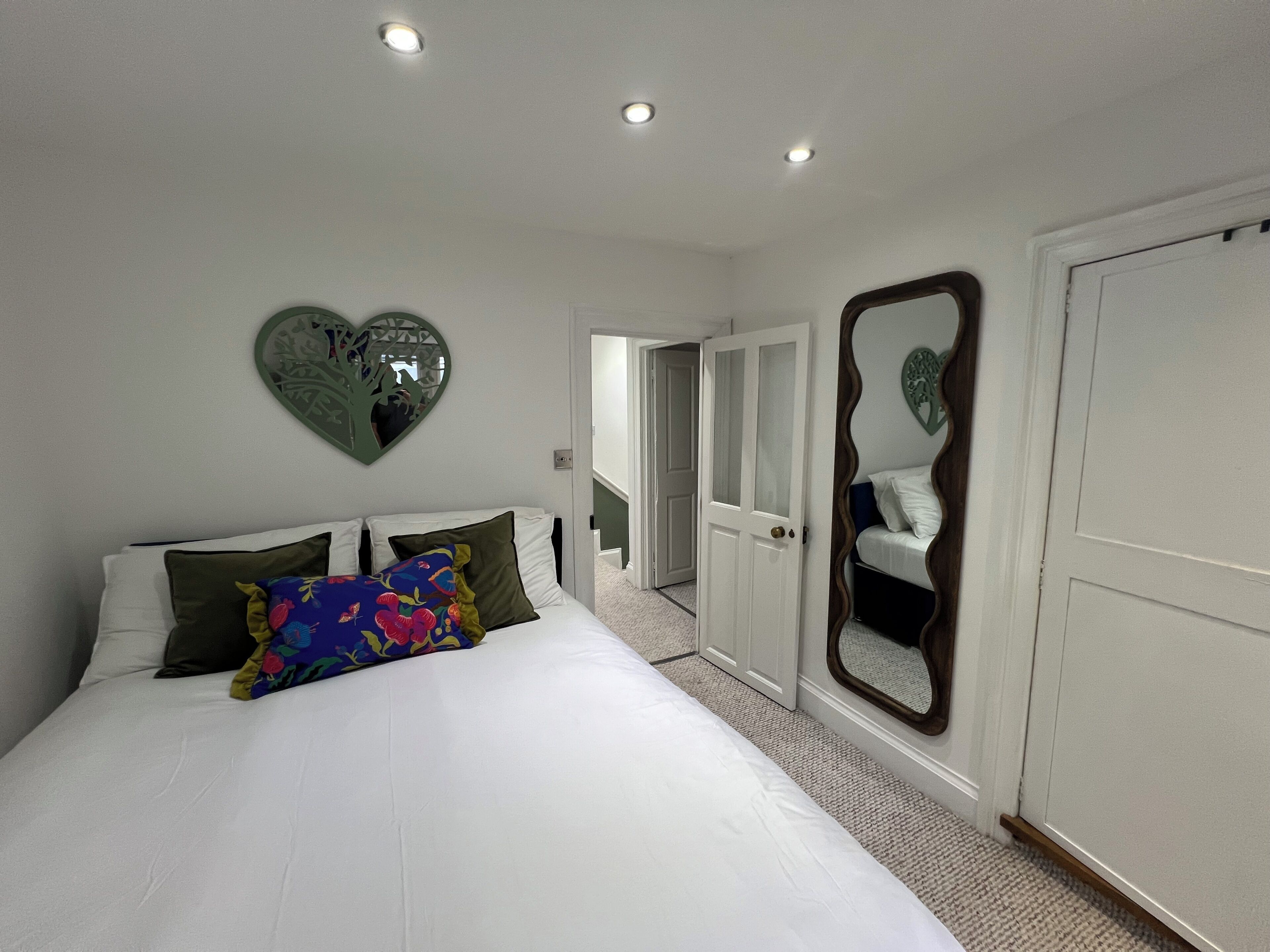 Een slaapkamer met een bed, een spiegel in de vorm van een hart en een deur naar een gang.