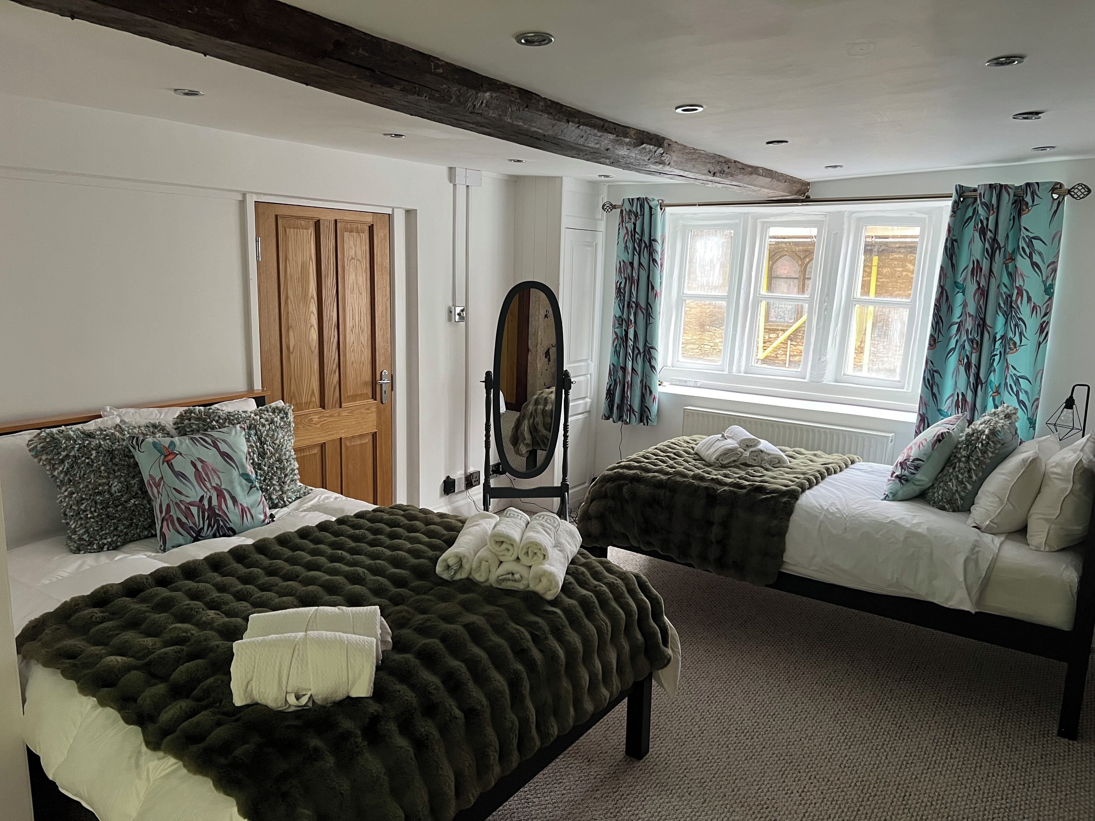 A bedroom with two beds, a wooden door, a mirror, and a window with curtains.