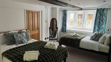 A bedroom with two beds, a wooden door, a mirror, and a window with curtains.