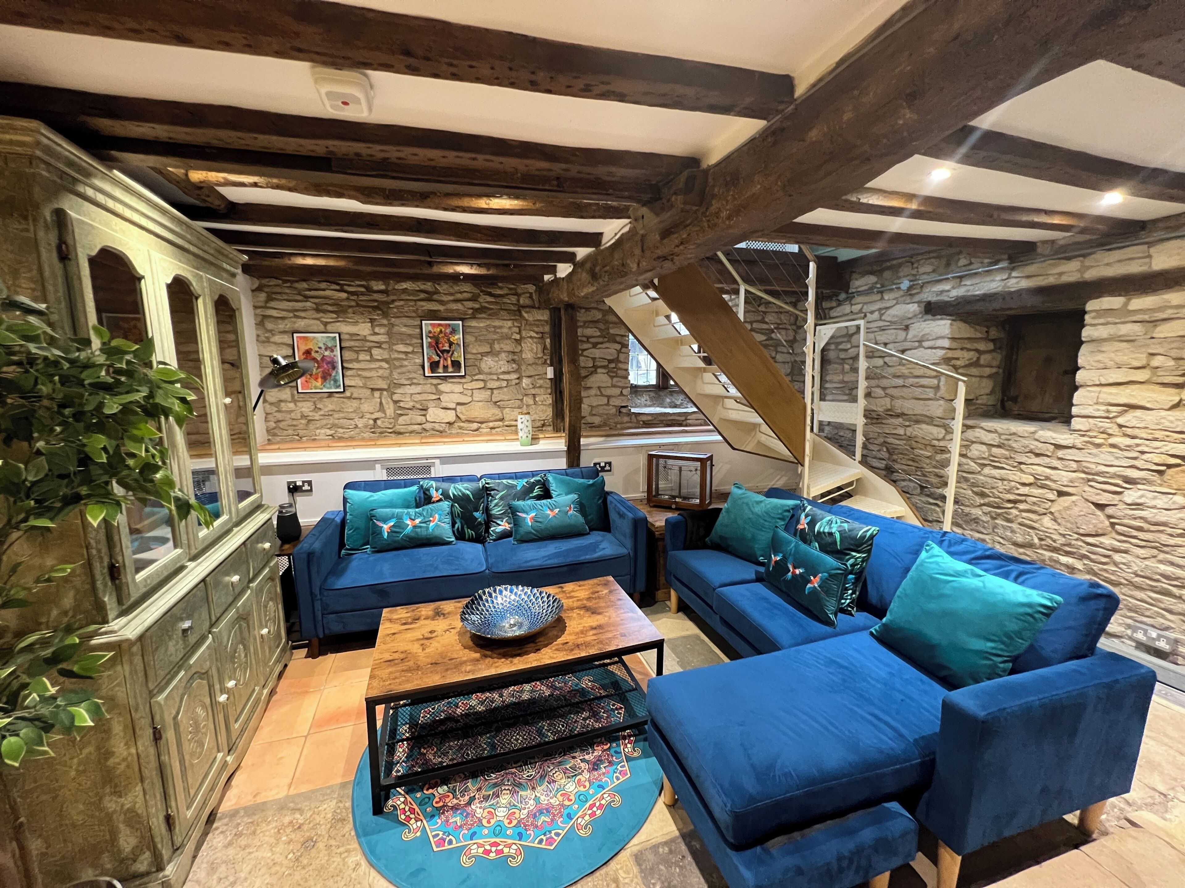 A cozy living room with blue sofas, a patterned rug, and a stone wall.
