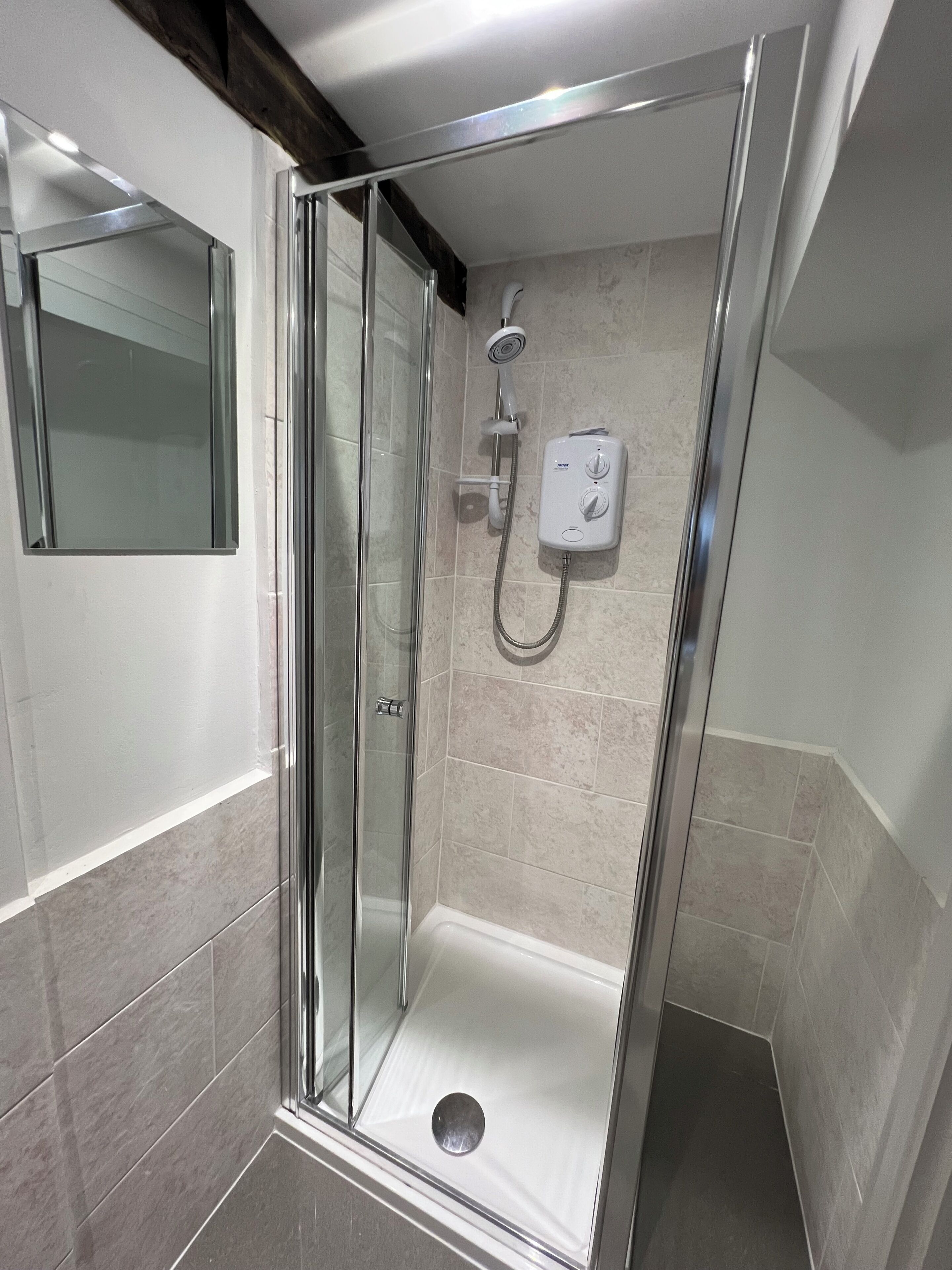 A glass-enclosed shower stall with a handheld showerhead and a control panel.