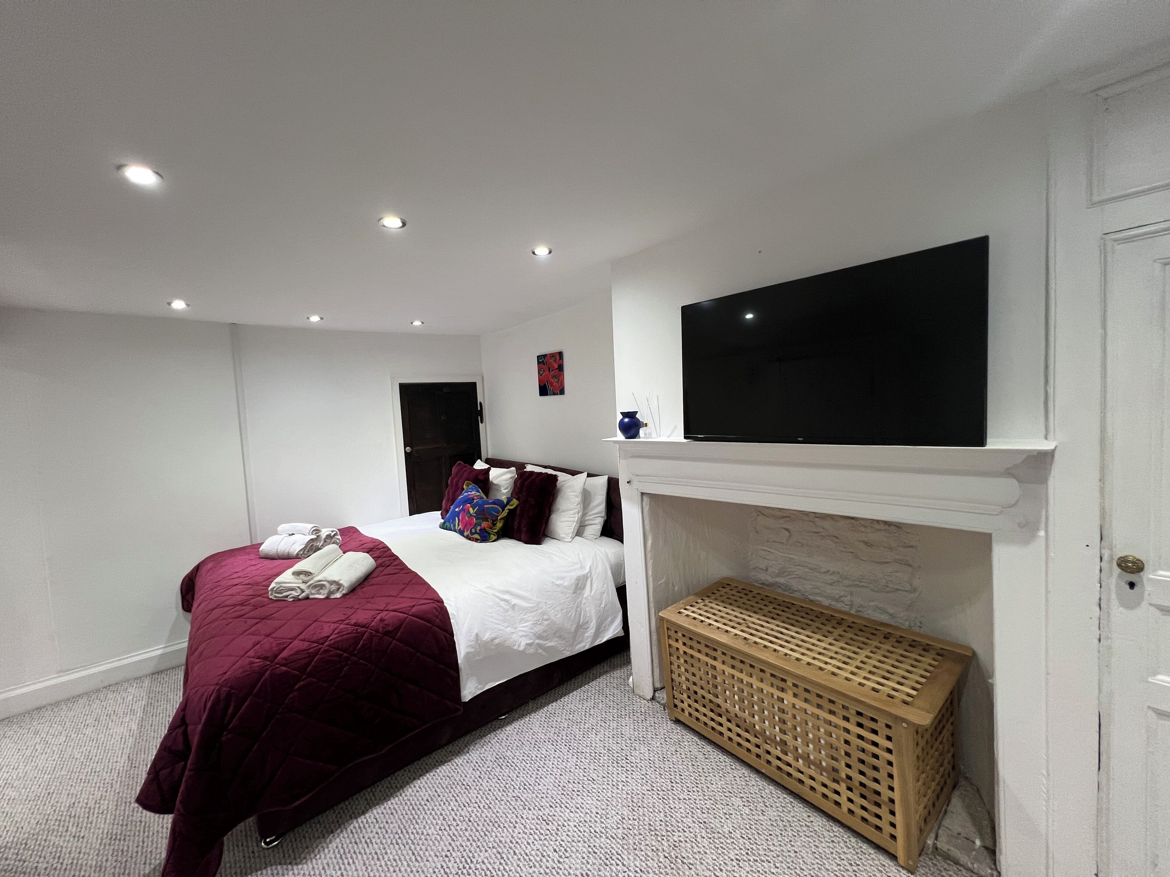 Un dormitorio con cama, televisor sobre la chimenea y una puerta.