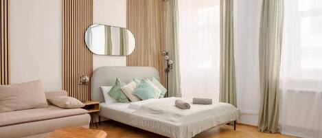 A modern bedroom with a bed, a sofa, a mirror, and a bedside table.