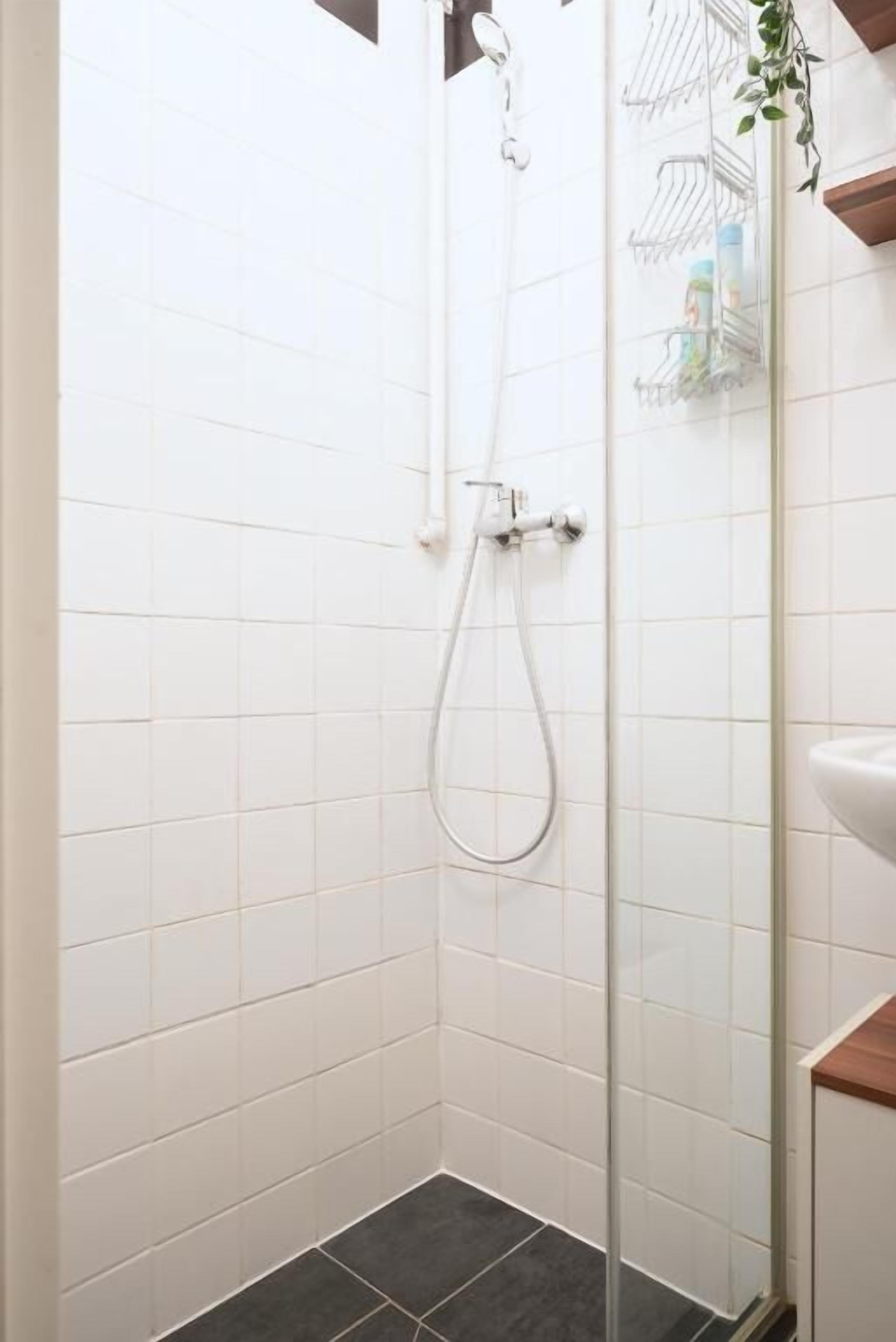 A shower area with white tiled walls, a glass door, and a showerhead.