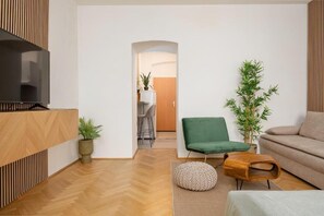 A modern living room with a TV, a green chair, a sofa, and a wooden coffee table. - An der Donau und 15 Minuten ins Zentrum (Wien)