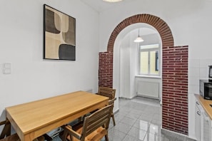 Un coin repas avec une table et des chaises en bois, une arche en briques et un espace cuisine équipé d’un four à micro-ondes.