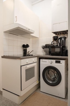 A compact kitchen with a built-in washer and dryer, a stove, and a coffee maker. - An der Donau und 15 Minuten ins Zentrum (Wien)