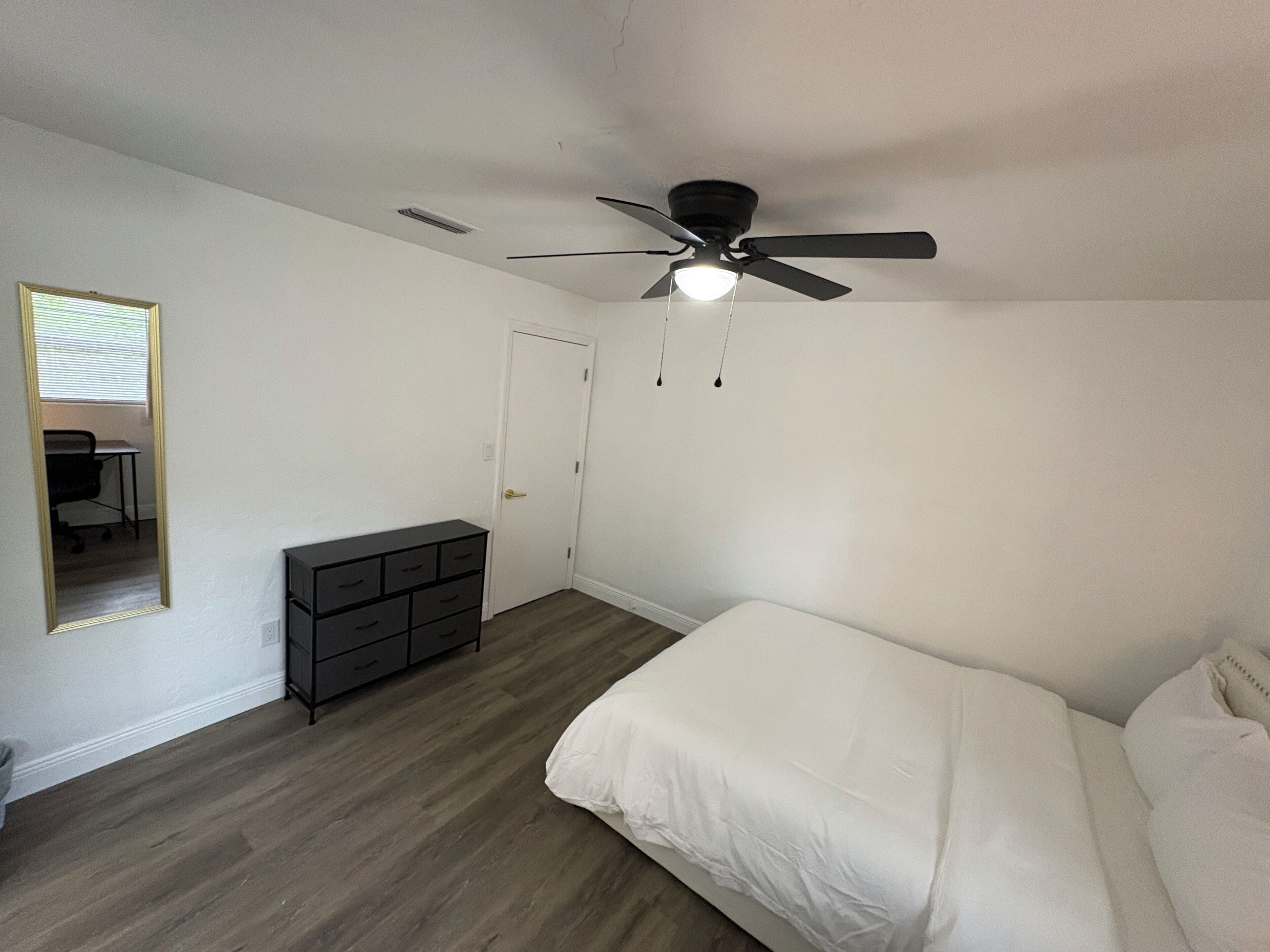 Un dormitorio con una cama, un aparador, un ventilador de techo y una puerta.
