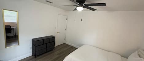 Un dormitorio con una cama, un aparador, un ventilador de techo y una puerta.