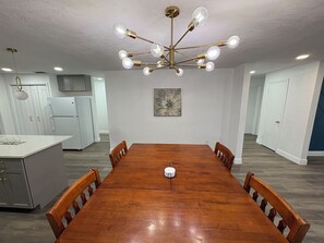 A dining room with a wooden table, chairs, a chandelier, and a kitchen in the background. - 3BR/2BA Modern & Spacious House Near UF - Great for Game Days or Commencements! (Gainesville)