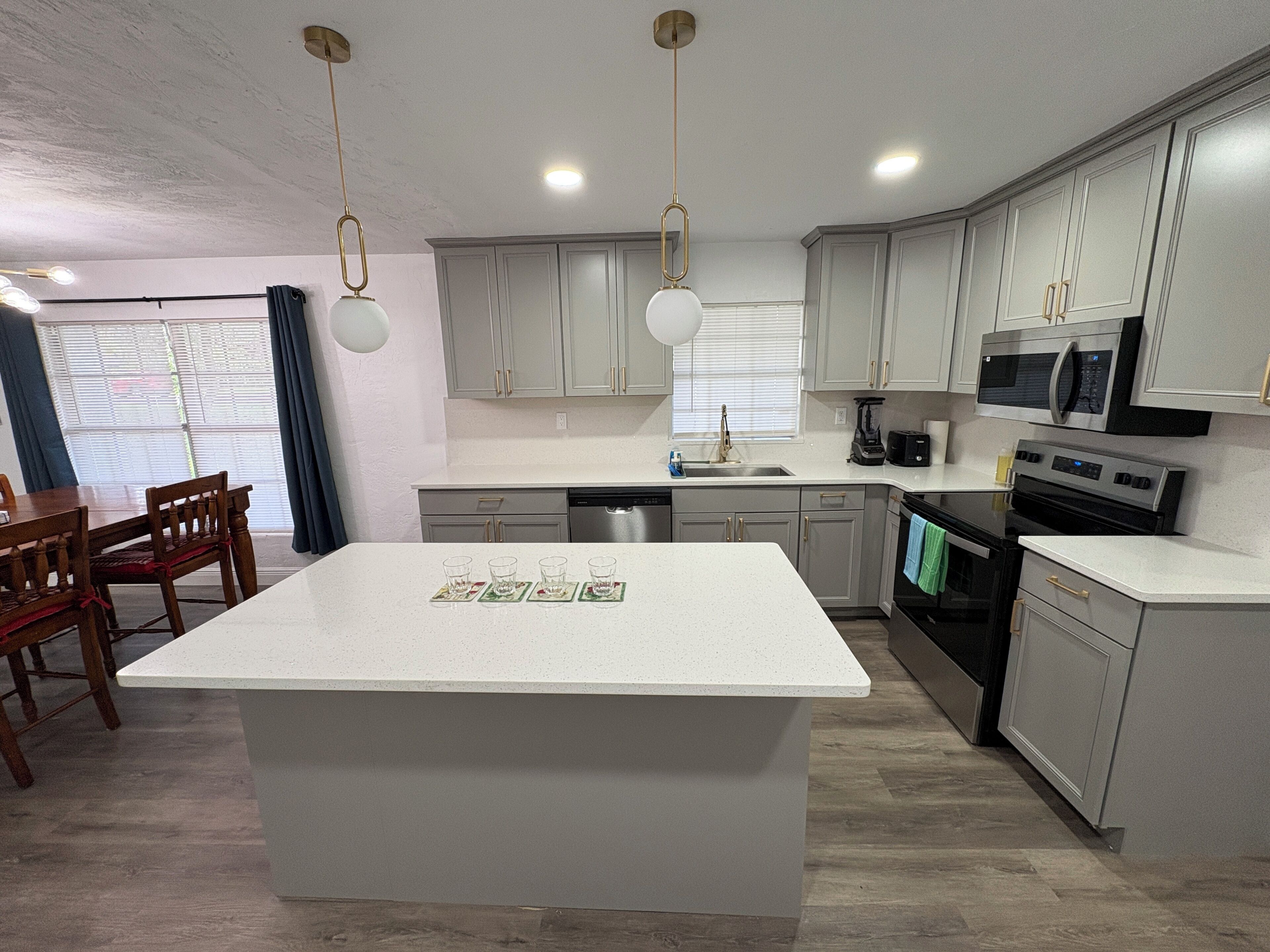 A modern kitchen with a central island, stainless steel appliances, and light grey cabinetry.