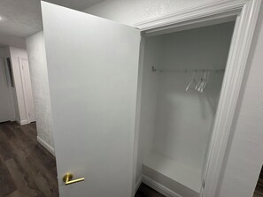 Ein Zimmer mit weißer Tür, einem Kleiderschrank mit Kleiderstange und Holzboden.