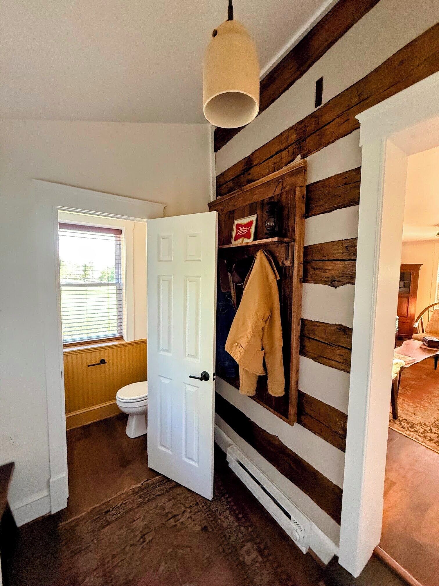 Ein Badezimmer mit einer Holzwand, einer weißen Tür, einer Toilette und einer Pendelleuchte.