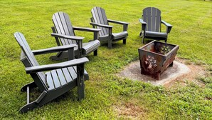 A grassy outdoor area with Adirondack chairs and a metal fire pit.