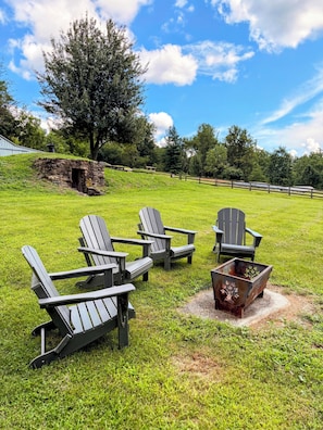 A grassy outdoor area with Adirondack chairs and a metal fire pit.