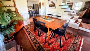 Uma sala de jantar com mesa de madeira, cadeiras pretas, tapete estampado em vermelho e luminária pendente verde.