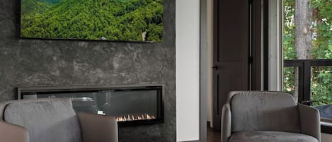 A modern living room with a fireplace, comfortable seating, and a large TV displaying a mountainous landscape.