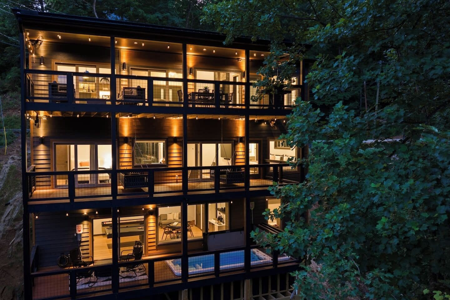 A multi-story building with a balcony on the upper level, a pool area on the ground floor, and a well-lit interior.