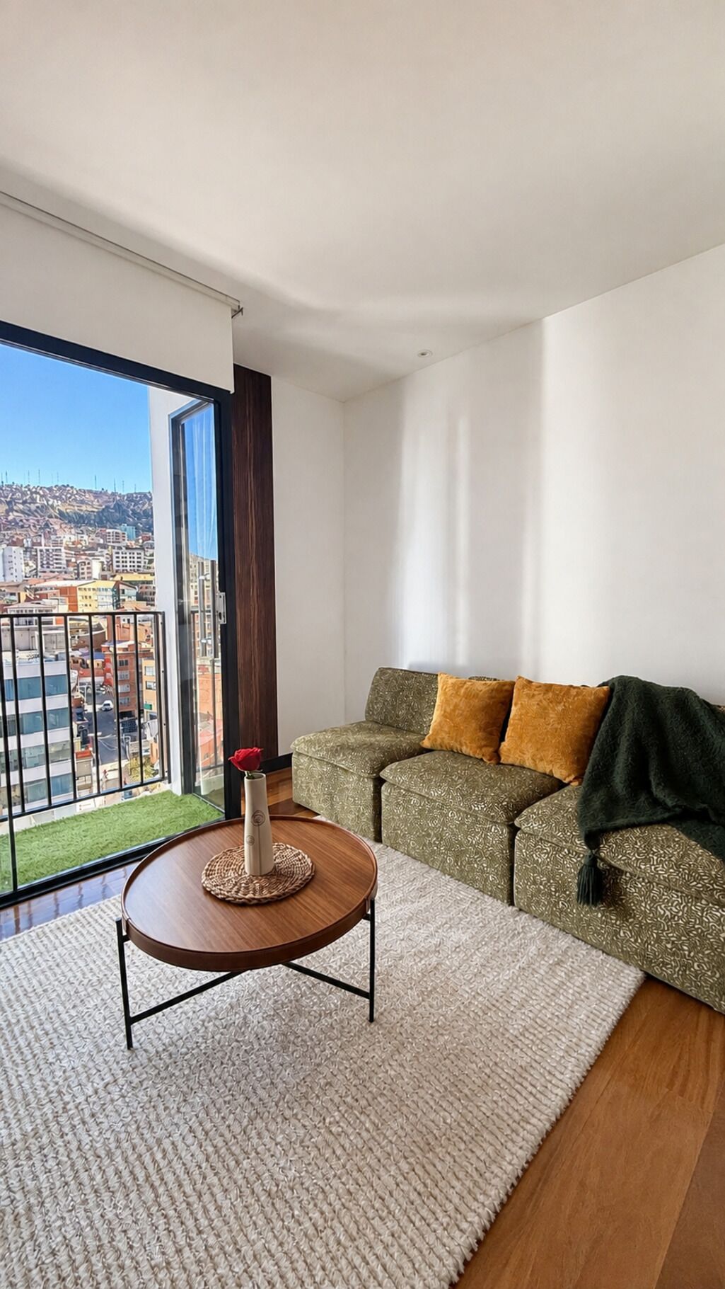 A modern living room with a sofa, a small round table, and a view of a cityscape through large windows.