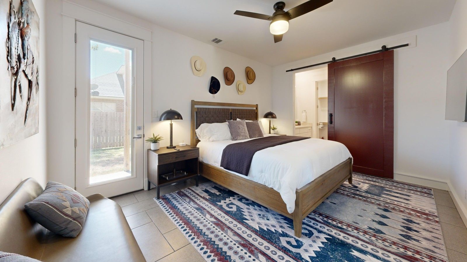 Une chambre à coucher avec un lit, des tables de chevet, un ventilateur de plafond et un tapis à motifs.