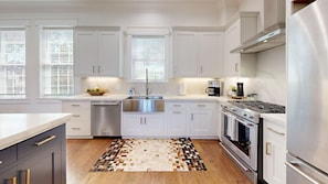 A modern kitchen with white cabinets, stainless steel appliances, and a patterned rug.