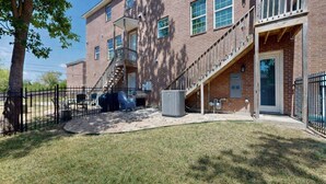 A brick building with a covered outdoor seating area, a staircase, and a fenced yard.