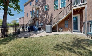 A brick building with a covered outdoor seating area, a staircase, and a fenced yard.
