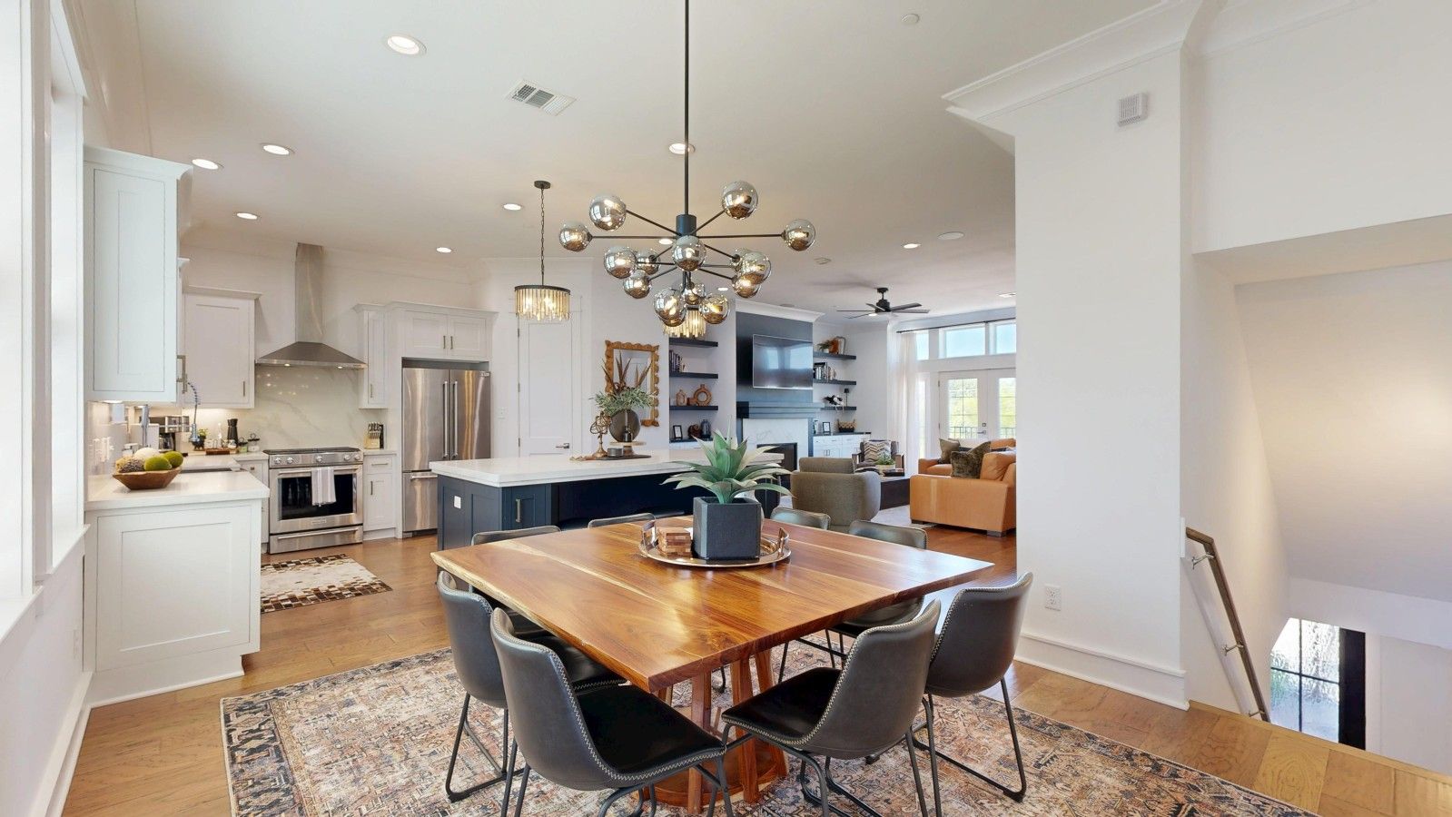 A spacious kitchen with modern appliances, a dining area with a wooden table and chairs, and a large chandelier.